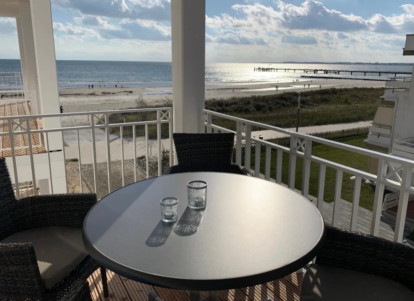 Balkontisch mit Gläsern, dahinter Strand, Seebrücke und Ostsee