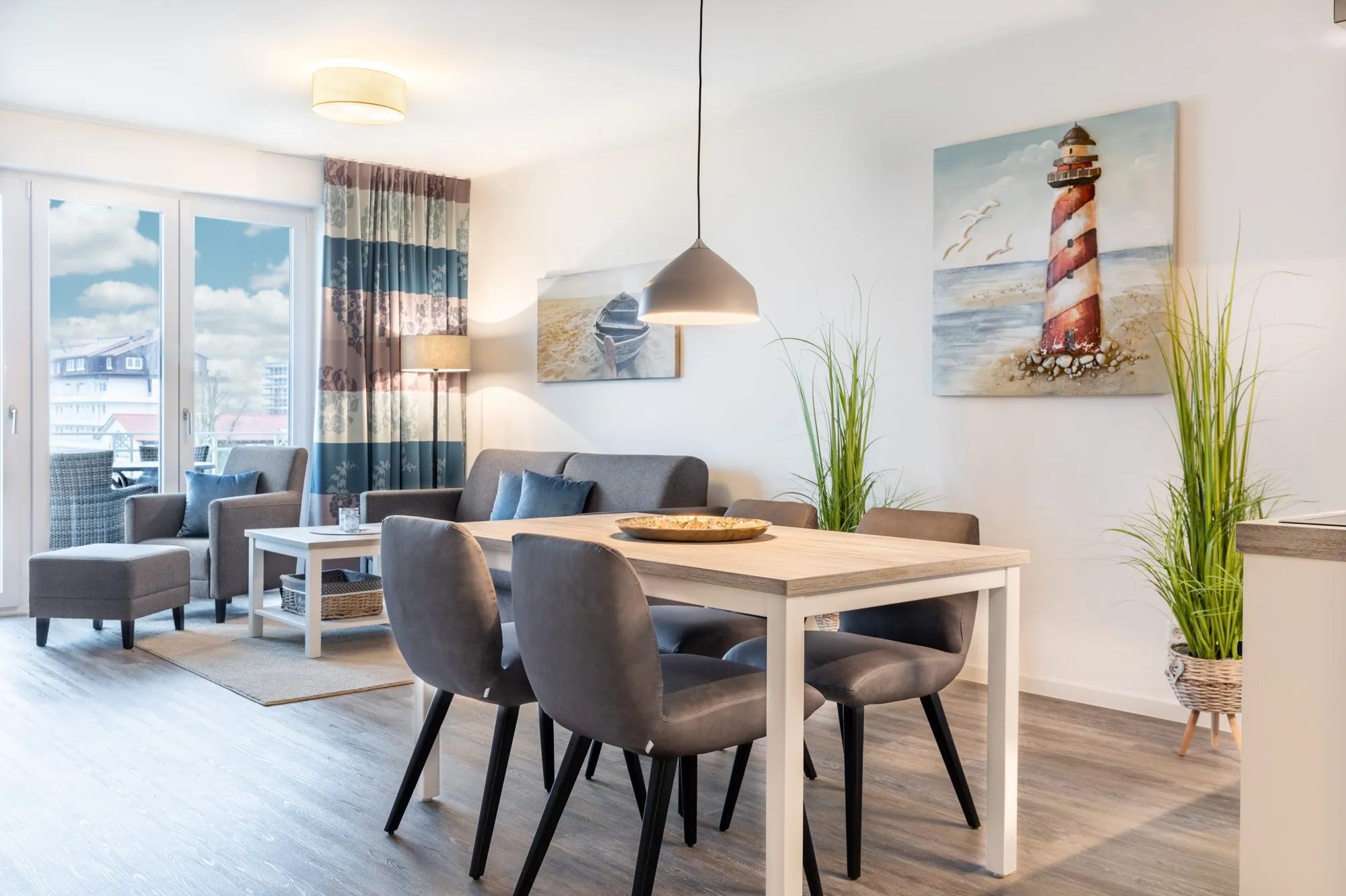Wohn- und Essbereich mit grauem Sofa, Esstisch und Leuchtturm-Bild